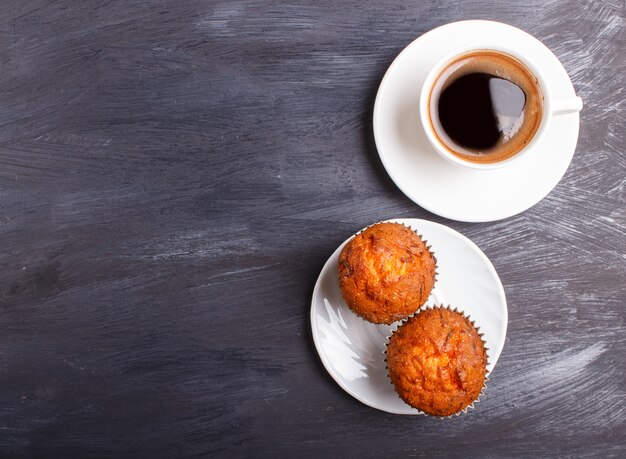 Two carrot muffins with cup of coffee on white plate on black wooden background