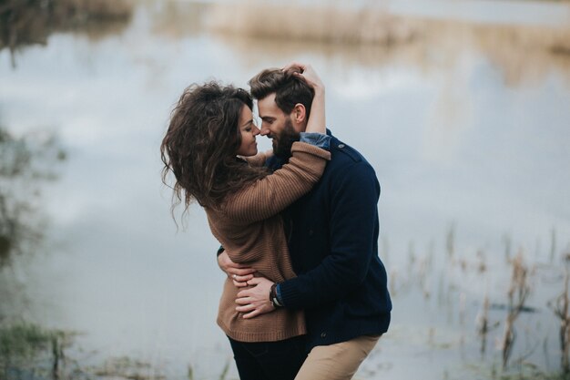 Two caucasian lovers near the lake. Young couple is hugging on autumn day outdoors. A bearded man and curly woman in love. Concept of love.