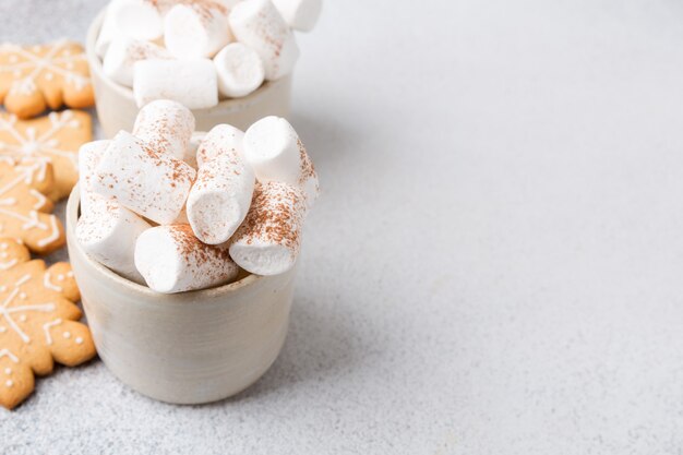 Two ceramic mugs of hot cocoa served with marshmallow on a gray background, copy space