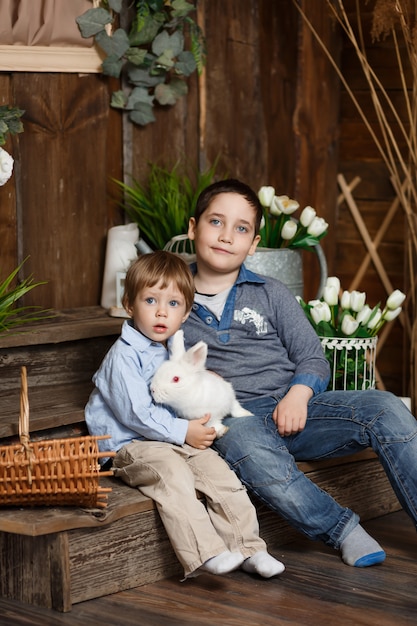 Two charming boys play with a white rabbit in a Studio with rustic decor. Funny and cute brothers