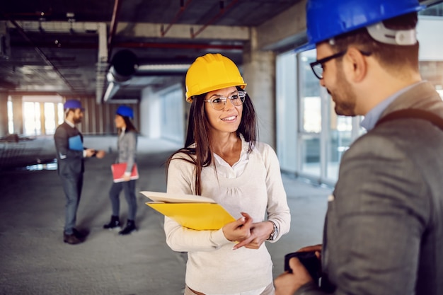 Two charming colleagues standing inside of building in construction process, chatting and taking a break from hard work.