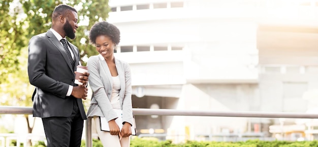 Two cheerful african american coworkers chatting outdoors during coffee break copy space