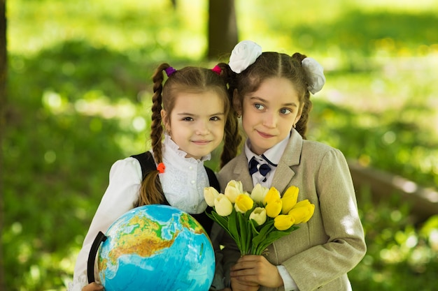 Two cheerful Caucasian girls schoolgirls with flowers and a globe