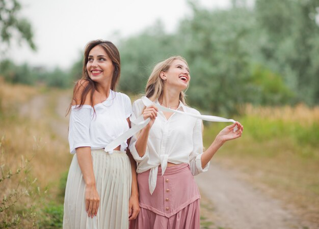 Photo two cheerful emotional best girlfriends in retro style clothes in retro clothes walk along the landing with the road on summer cloudy day. walk together