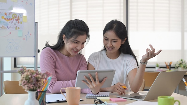 Two cheerful female start up business colleagues sharing information and discussing new project together