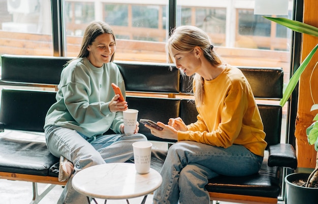 Photo two cheerful laughing women friends in a coffee shop communicate and chat on the phone