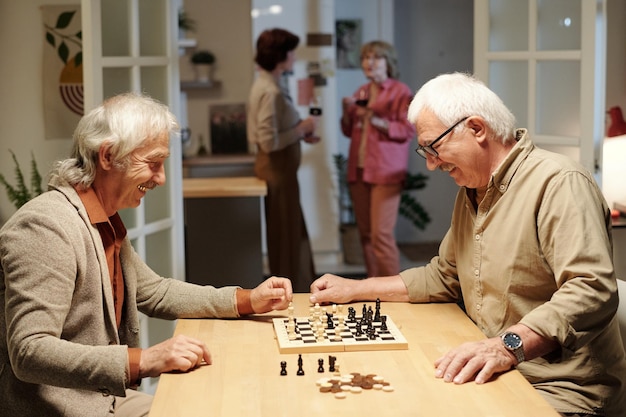 Two cheerful retired men in casualwear looking at chessboard with figures