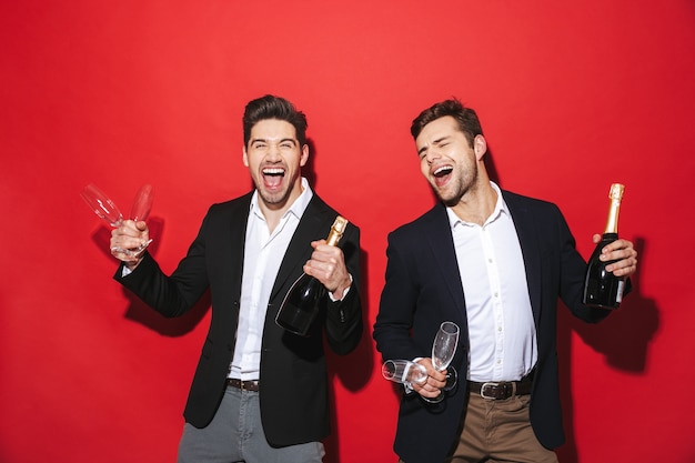 Two cheerful smartly dressed men standing isolated over red space, celebrating New Year