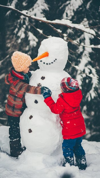 Photo two children one in a red jacket and one in a plaid jacket build a snowman in the snow