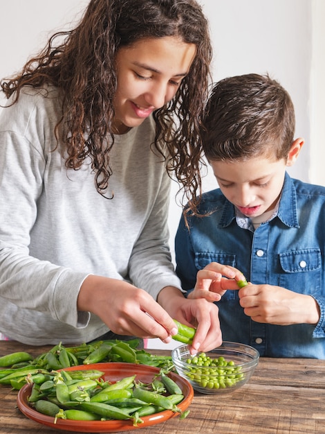 Two children removing fresh peas from their pods