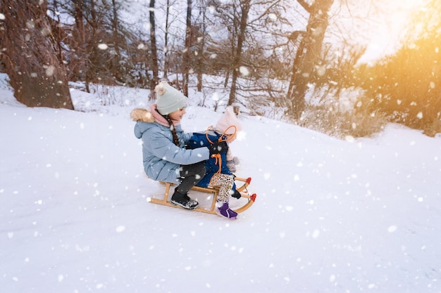 Two children ride on wooden retro sled on sunny winter day active winter outdoors games winter