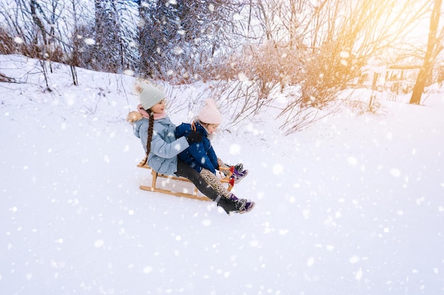 Two children ride on wooden retro sled on sunny winter day active winter outdoors games winter