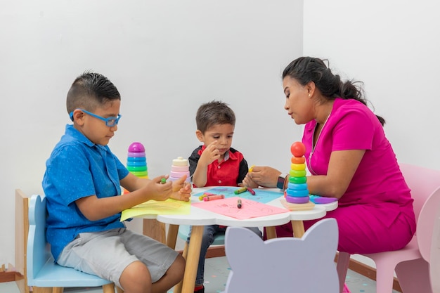 Two children sitting at a table drawing with their pediatrician doctor on a table in the office