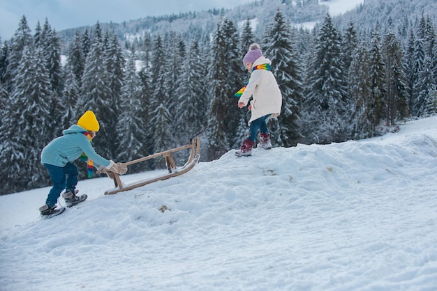 Two children sledding with mountain winter day. Little kids playing outdoors in the snow.