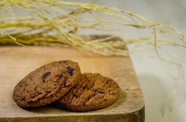 Two chocolate chip cookies on a wooden cutting board