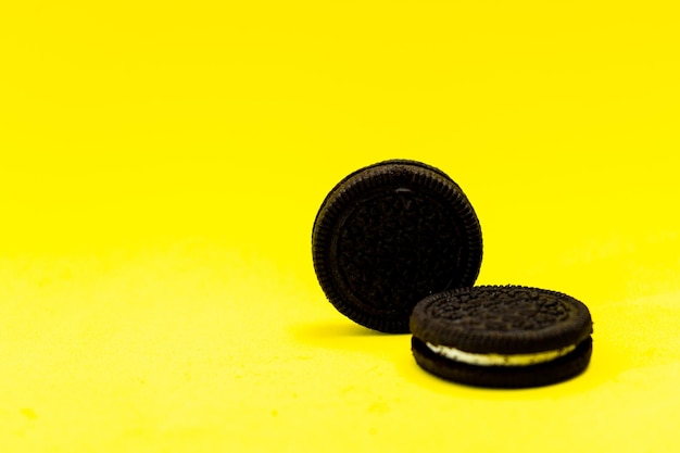 Two chocolate sandwich cookies with sweet cream on a pure yellow surface Copy space