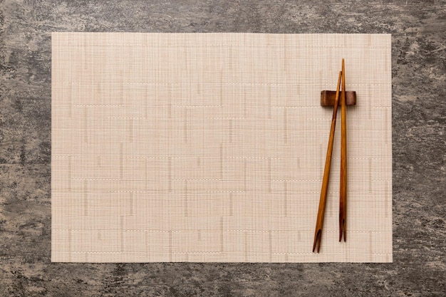 Two chopsticks and bamboo mat on cement background Top view copy space