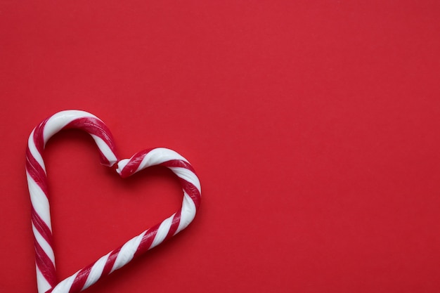 Two Christmas candy canes forming a heart shape on red background