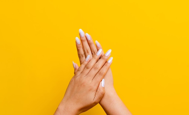 Two clean white hands and beautiful nails intertwined on a yellow background