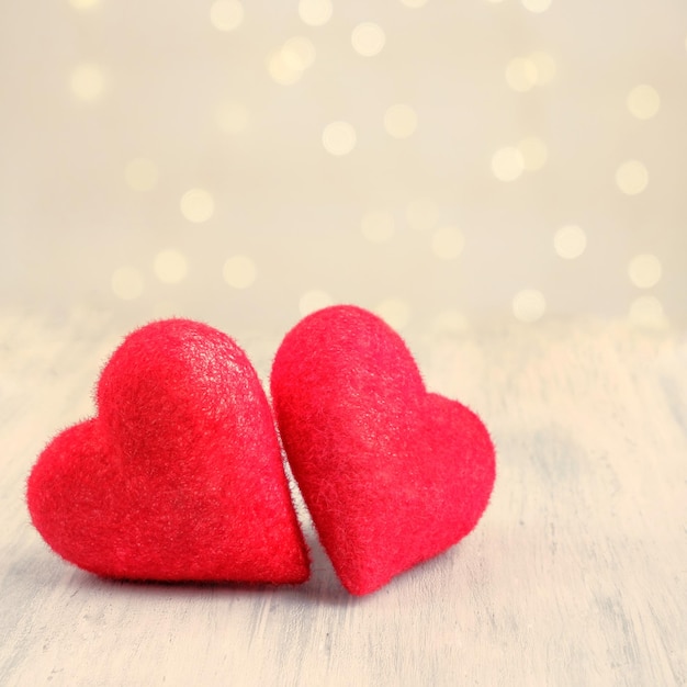 Two closeup love hearts on a wooden table and blurry defocused light bokeh background