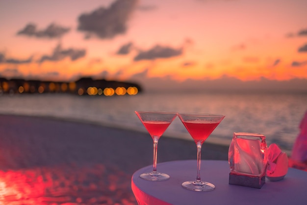 Two cocktail drinks with blur beach party people and colorful sunset sky in the background. Luxury