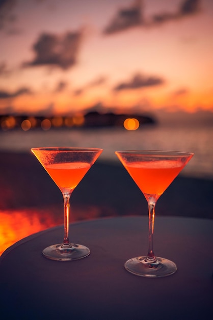 Two cocktail drinks with blur beach party people and colorful sunset sky in the background. Luxury