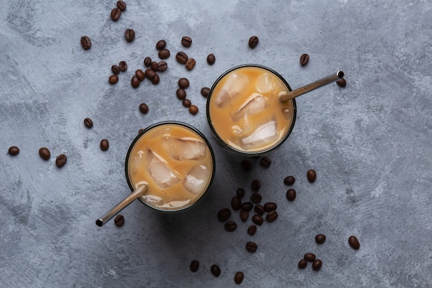 Two cold coffee in a glass cup with a metal straw, coffee beans on a gray concrete space