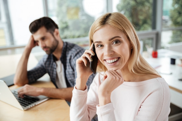 Two colleagues in office. Woman talking by phone.