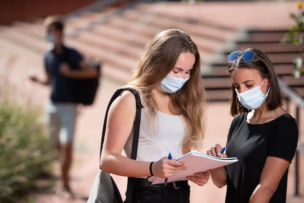 Two college student girls wearing a face mask looking at a notebook