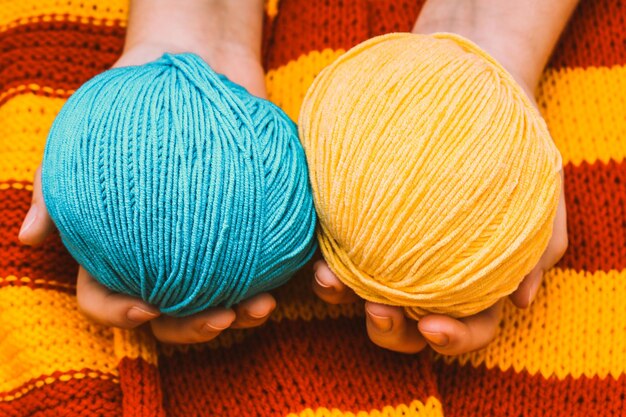 Two colored skeins of wool in hands on a yellow-red knitted tablecloth. High quality photo