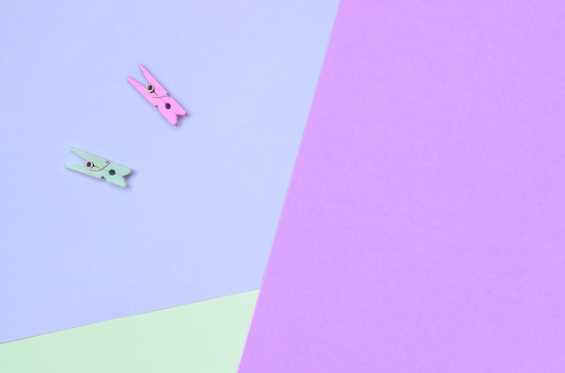 Two colored wooden pegs lie on texture of fashion pastel violet, turquoise and pink colors paper