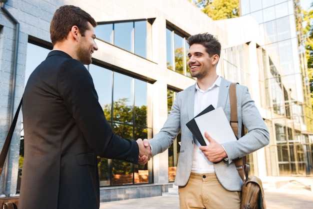 Two confident businessmen standing outdoors, shaking hands