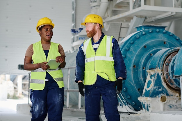 Two confident engineers in workwear and hardhats discussing working points