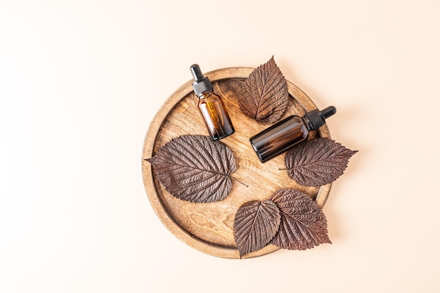 Two cosmetic bottles with an amber glass pipette with a natural antiaging face and body care product on a wooden tray among the autumn brown leaves