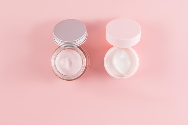 Two cosmetic jars with a delicate cream for the care of young skin on a pink background Open jar A copy of the space Natural cosmetics Top view