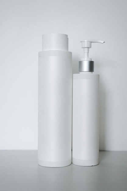 Two cosmetic plastic bottles with pump dispenser isolated on grey background