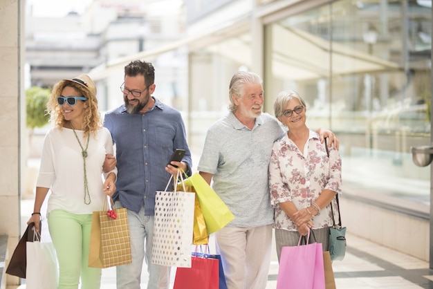 Two couples of two adults and two seniors go shopping together at the mall with a lot of bags with clothes and more on their hands - four people happy enjoying