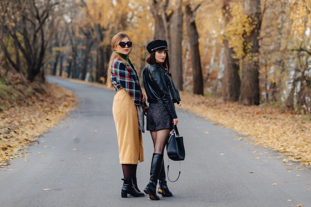 Two cozy smiling young girls walk at autumn park road