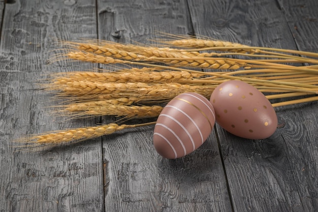 Two creatively colored Easter eggs and ears of bread on a wooden table Minimal Easter concept