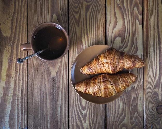 Photo two croissants and a cup of tea in a brown bowl on a wooden table