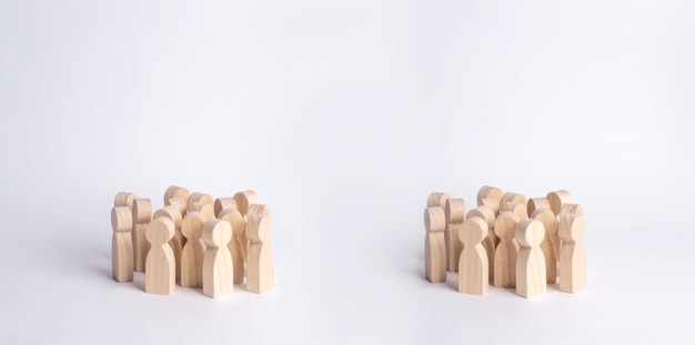 Two crowds of wooden figures of people are standing on a white background. 