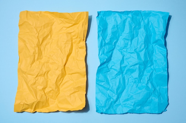 Two crumpled sheets of paper yellow and blue on a blue background space for an inscription