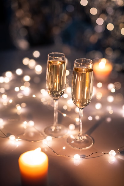 Photo two crystal flutes of sparkling champagne on table surrounded by lit garlands and burning candles in festive environment