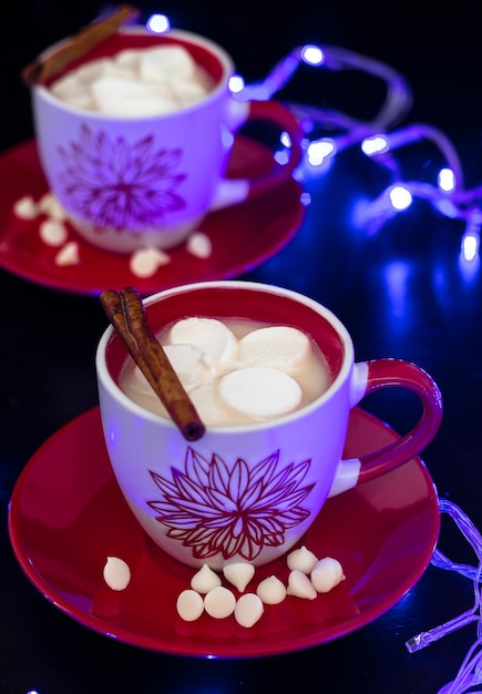 Two cup hot white chocolate with marshmallow on red plate Black and lighting blue background