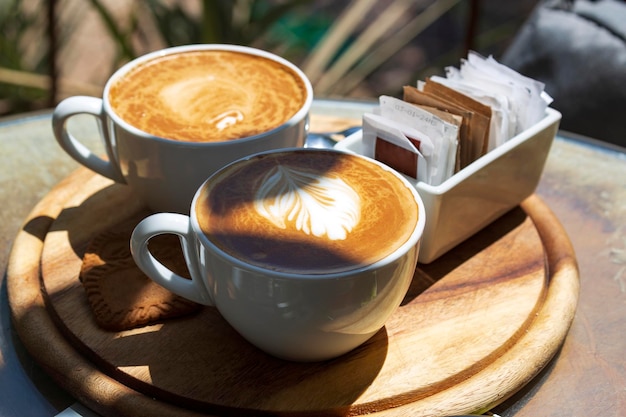 Two cups of cappuccino with latte art on wooden table in the morning at direct sunlight Selective focus Inspirational early morning breakfast with coffee Espresso latte coffee cups on wood tray