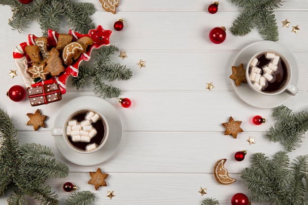 Two cups of cocoa with marshmallows and christmas cookies in a new years setting on a white wooden