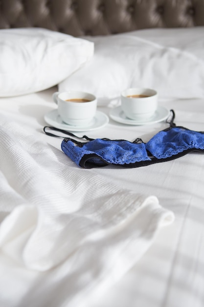 Two cups of coffee and a beautiful bra on a white bed closeup