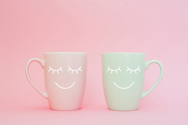  Two cups of coffee stand together to be heart shape on pink background with smile face