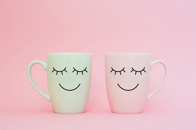  Two cups of coffee stand together to be heart shape on pink background with smile face