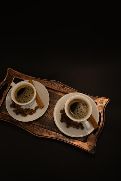 Two cups of coffee with cinnamon sticks on a tray